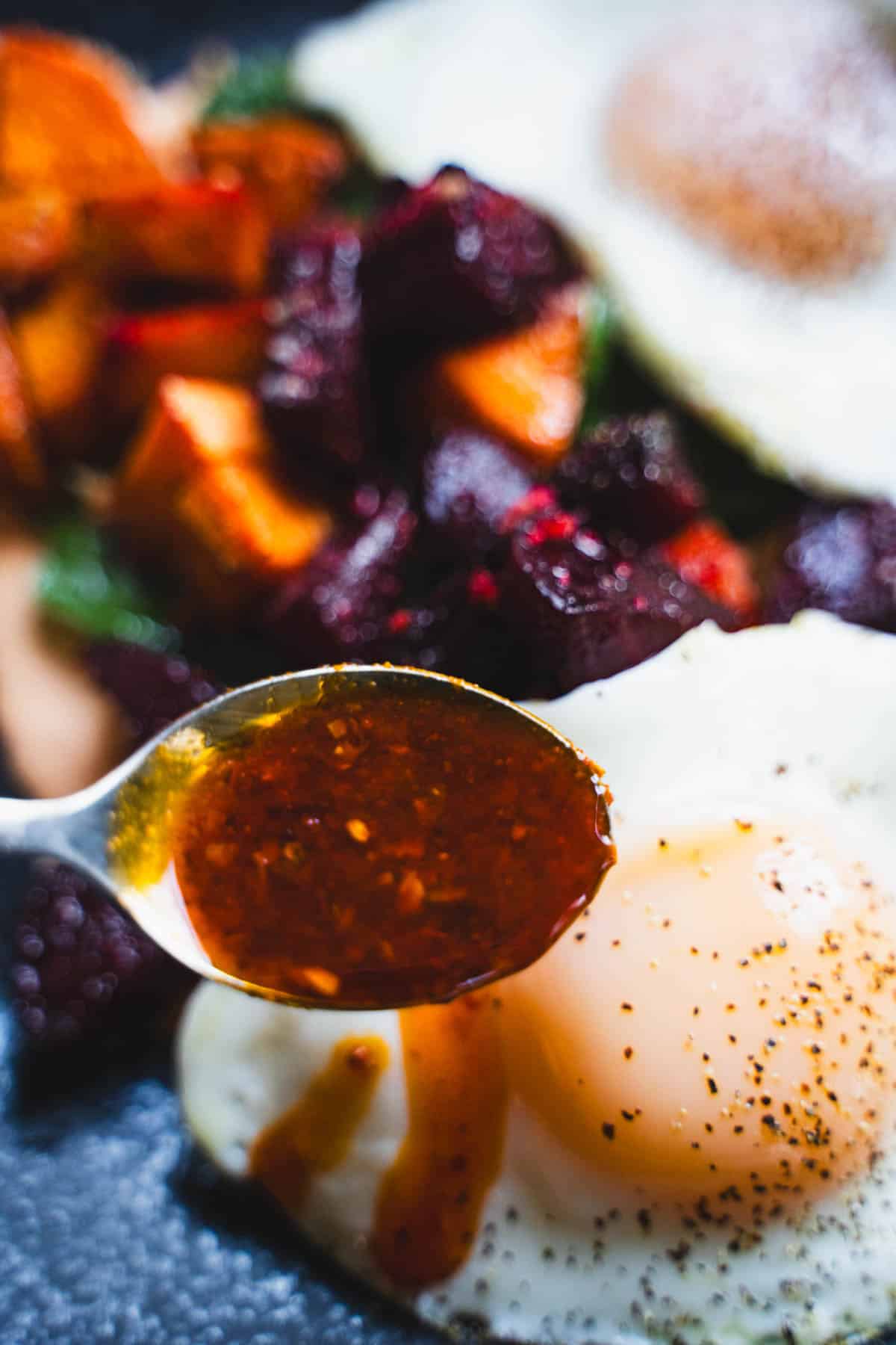 Chili crisp on a teaspoon garnishing the eggs for the roasted beets and sweet potato hash with eggs sheet pan breakfast.