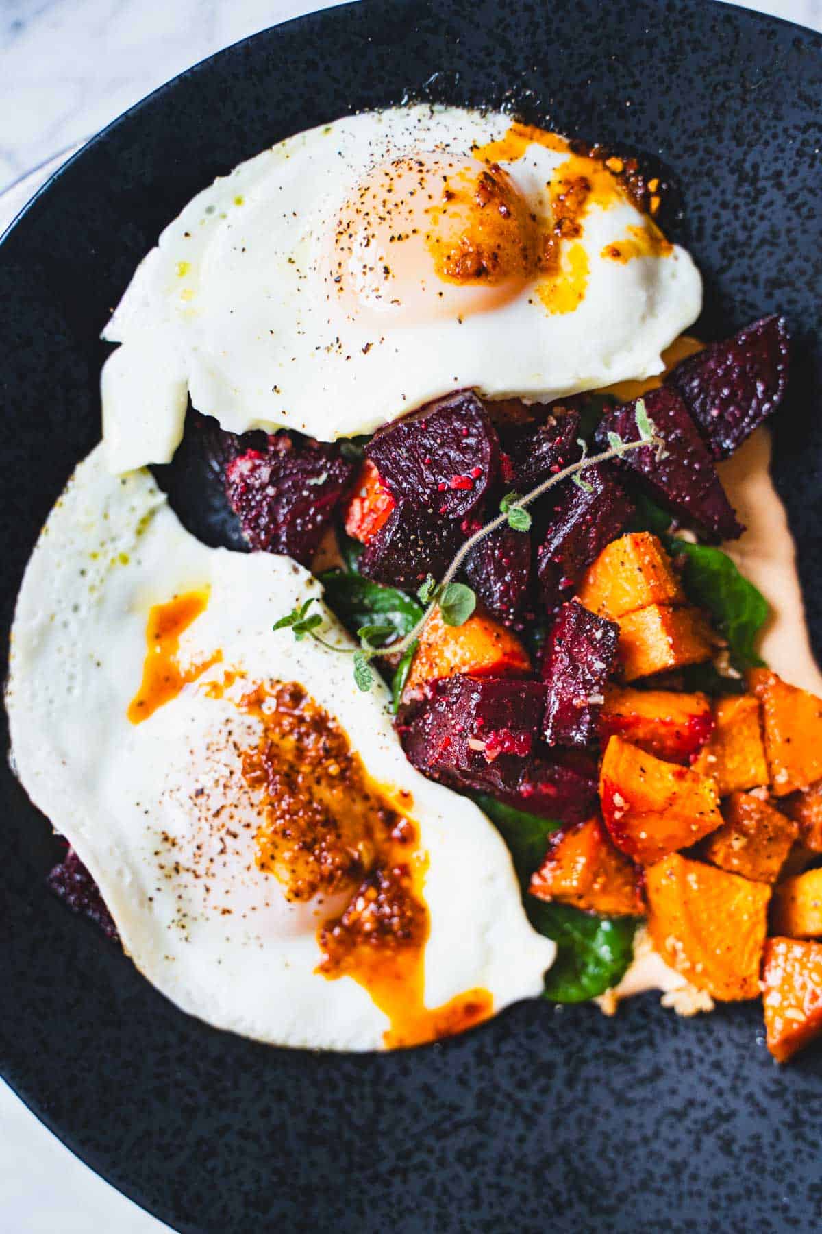 Roasted Beet and Sweet Potato Hash on a bed of spinach and chipotle mayo topped with two fried eggs.