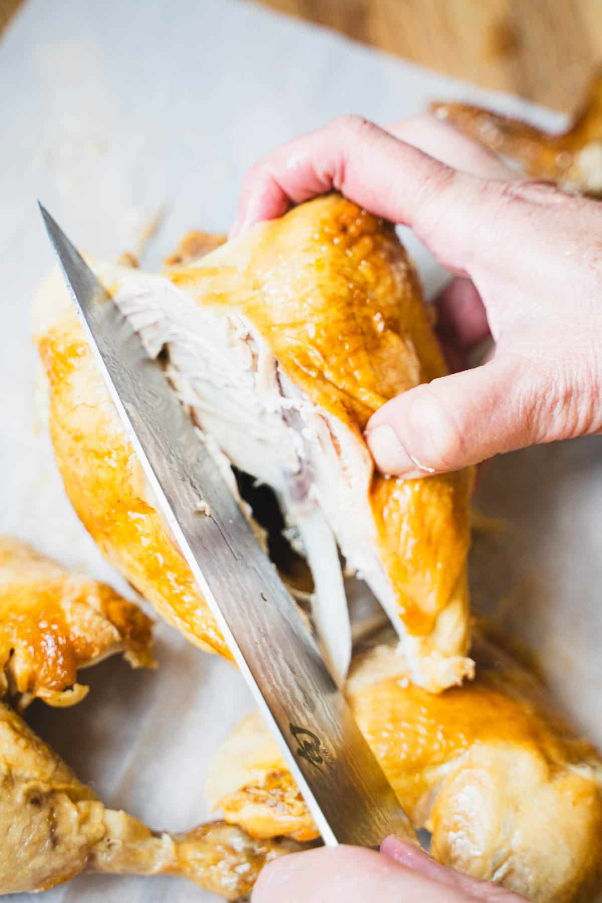 Knife running along breastbone and rib cage of rotisserie chicken.