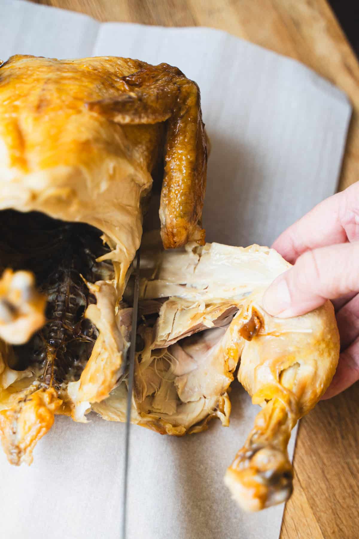 one hand holding the leg quarter and one hand holding knife to separate leg quarters from breast to carve the rotisserie chicken.