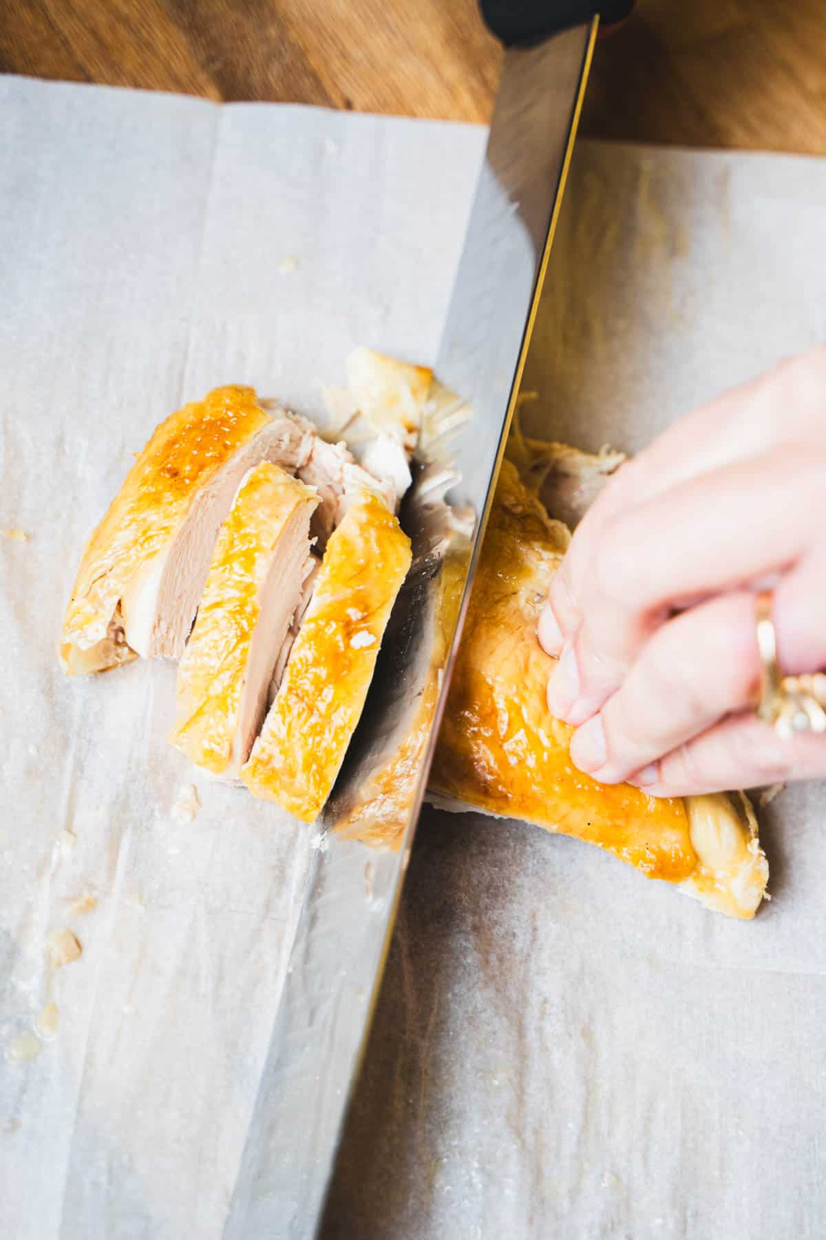 A slicing knife is cutting breast meat into ½ inch slices on parchment paper.