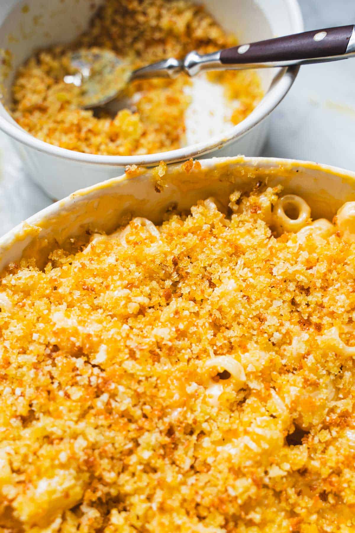3 cheese mac and cheese with panko in a white ramekin next to a bowl and spoon with toasted panko.