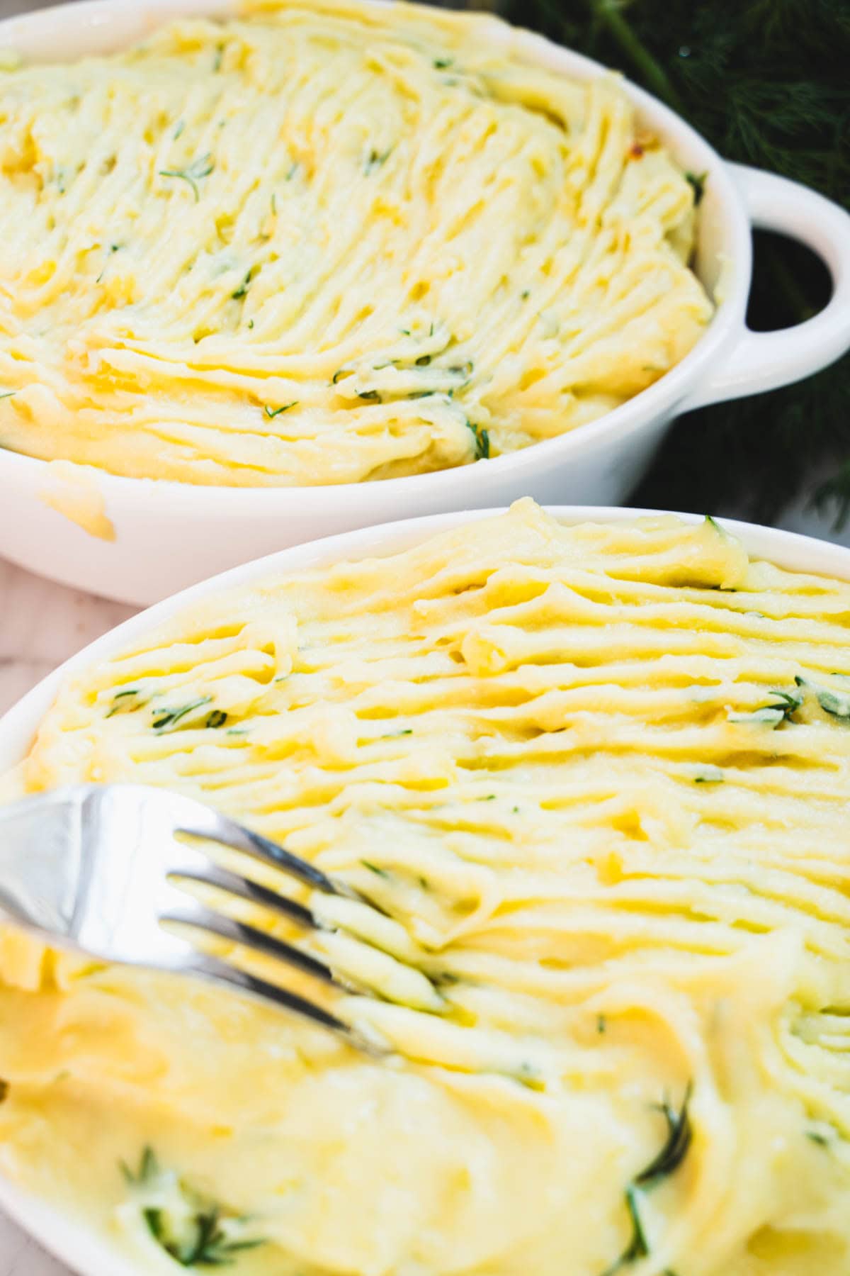 A fork being run across mash topping surface to create ridges in the individual seafood pot pie.