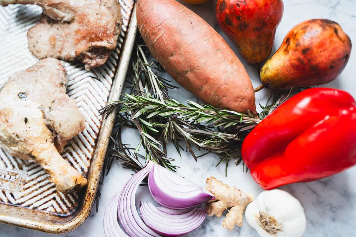 Ingredients for a Sheet Pan dinner of duck leg confit on baking sheet and marble counter.