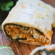 Baked chile releeno burrito on cutting board sliced open to see chile relleno, rice an bean filling with baked cheese on top.