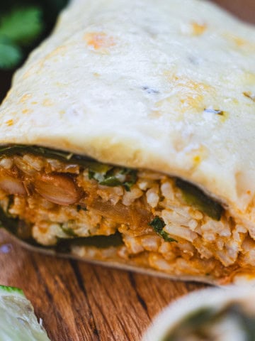 Baked chile releeno burrito on cutting board sliced open to see chile relleno, rice an bean filling with baked cheese on top.
