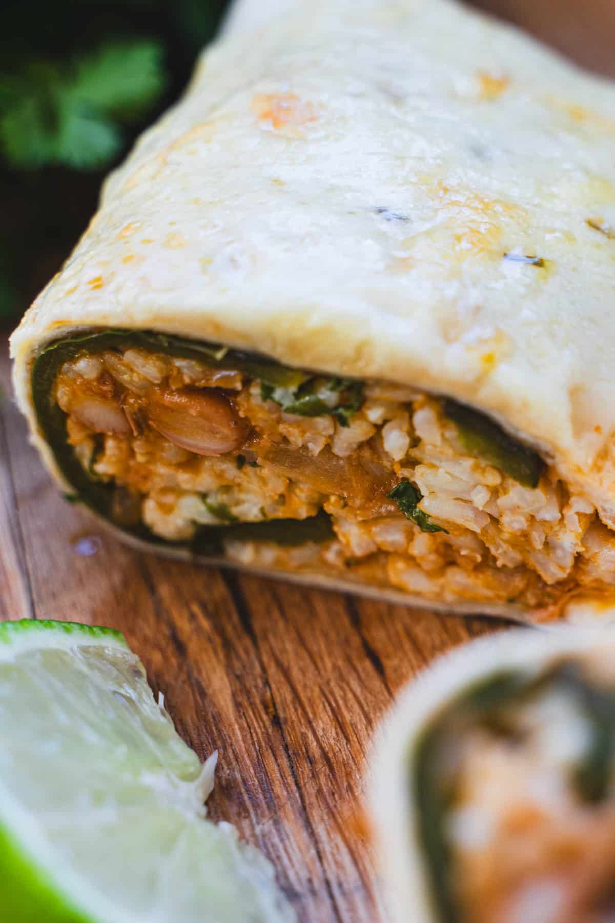 Baked chile releeno burrito on cutting board sliced open to see chile relleno, rice an bean filling with baked cheese on top.