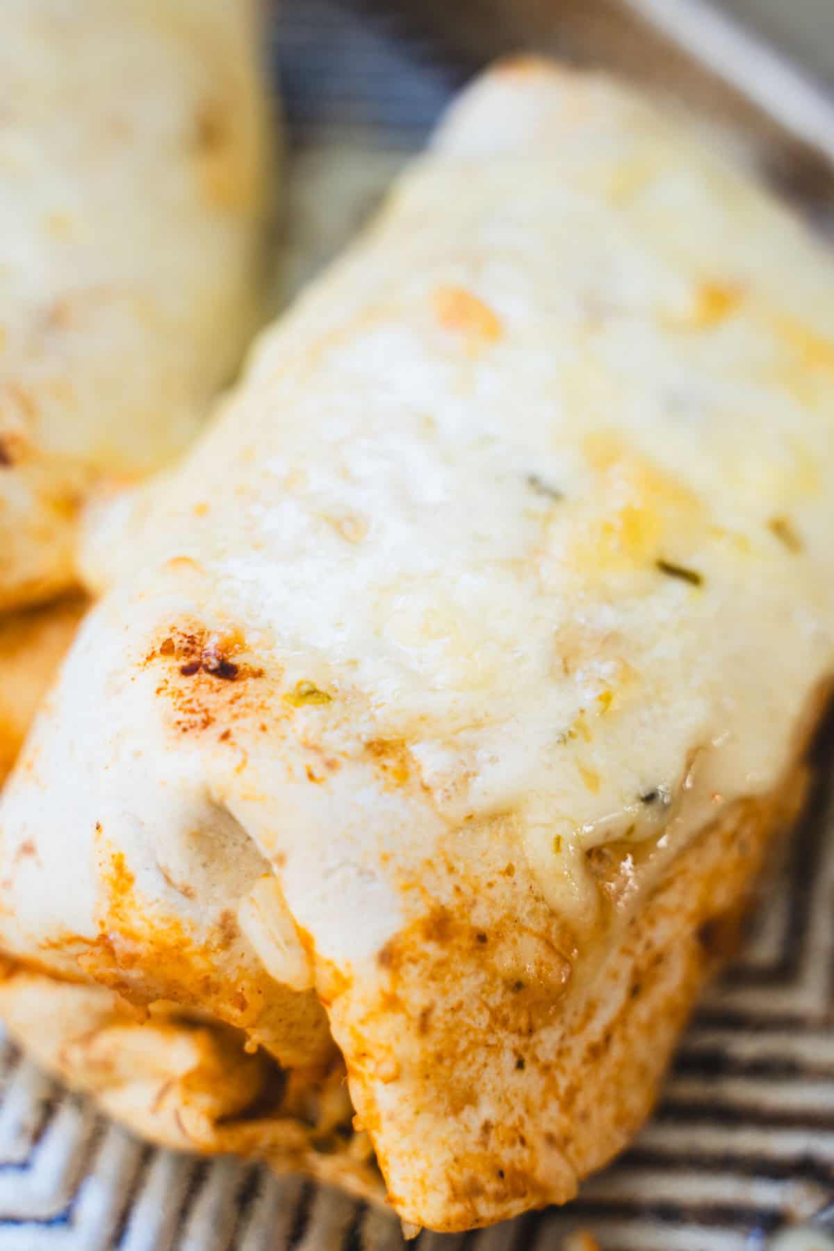 Baked chile relleno burrito with bean and rice filling and melted cheese on top on a baking sheet.