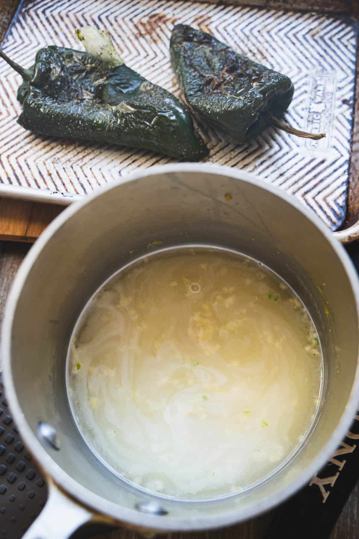 Rice and broth in sauce pan next to roasted chile relleno peppers on a baking sheet.