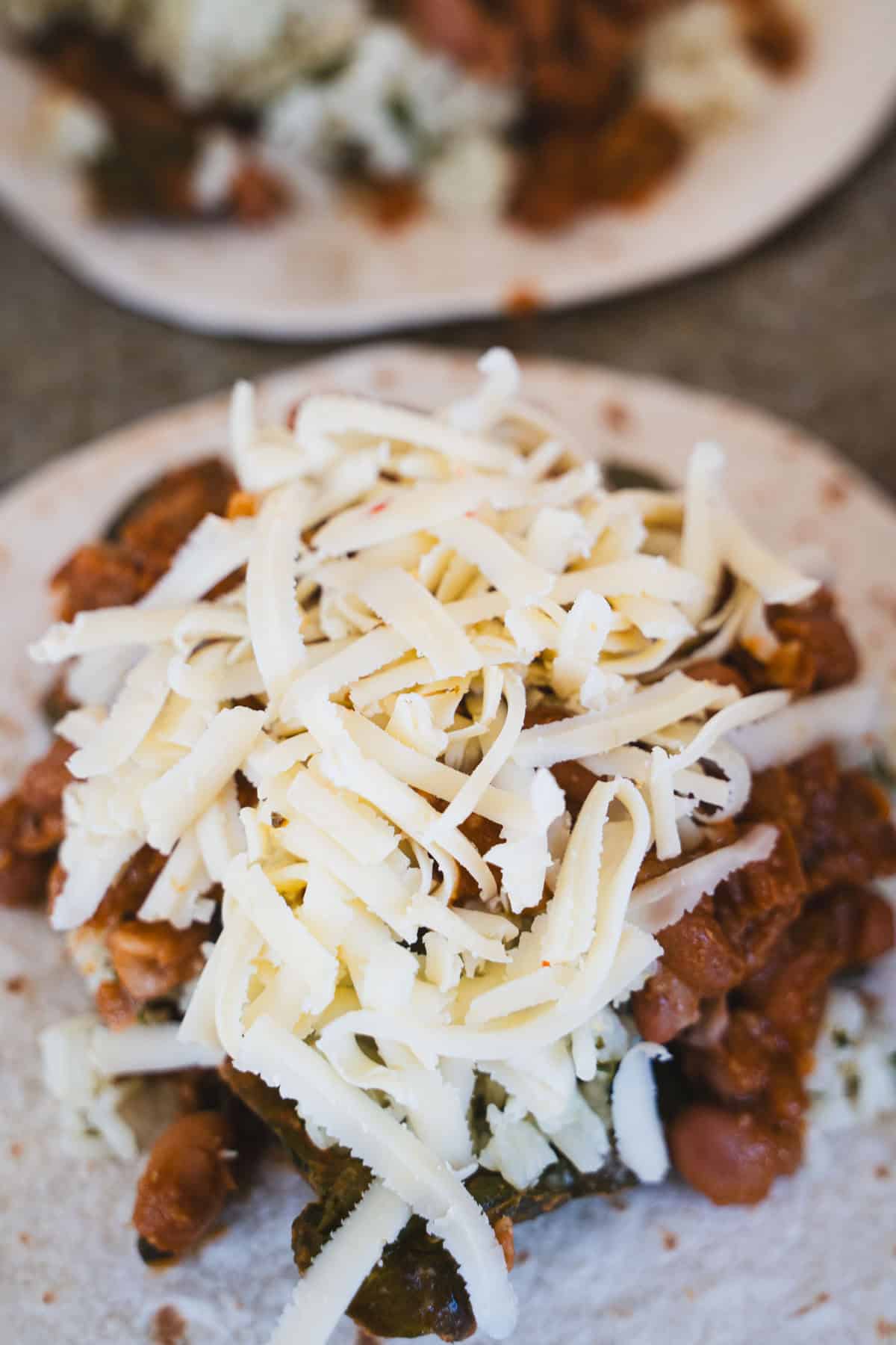 Last layer of shredded cheese on tortilla for baked burrito dinner for two.
