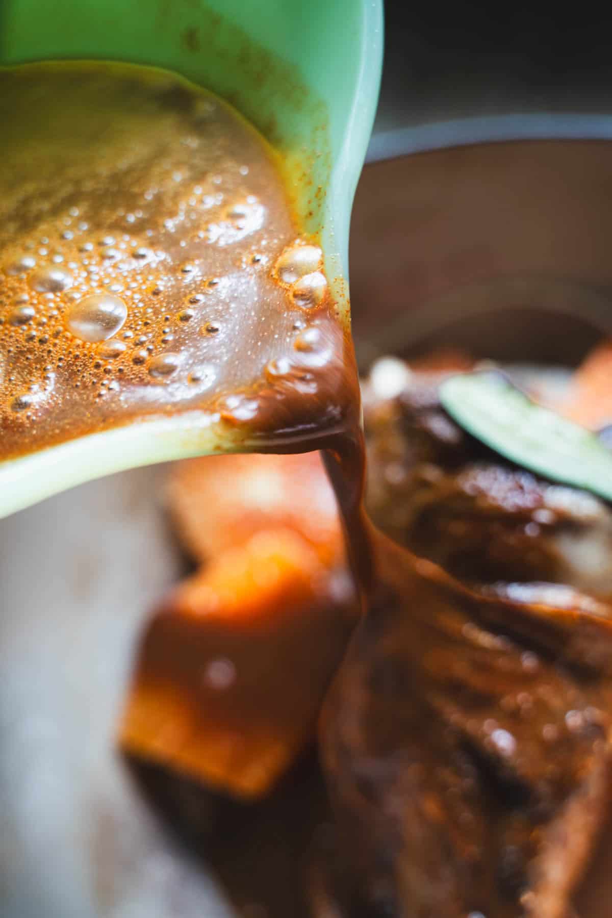 Barbacoa marinade being poured over lamb shanks, onions and orange slices in a dutch oven.
