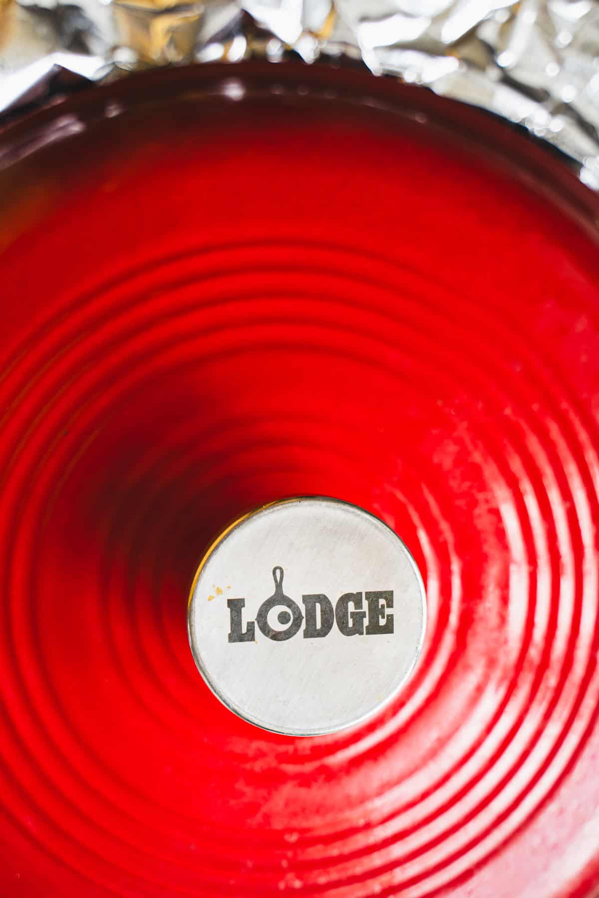 Dutch oven with aluminum foil and a red lid over the pot.