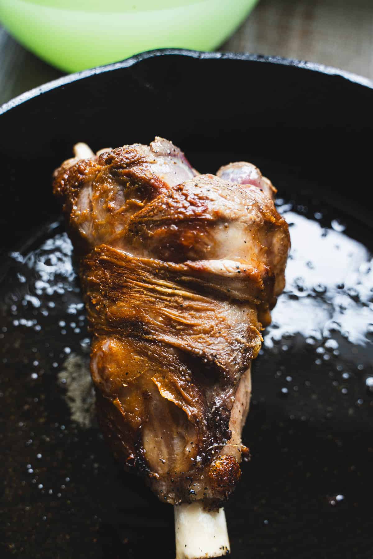 Lamb shank seared on all sides in a black cast iron skillet for lamb barbacoa with mexican green rice.