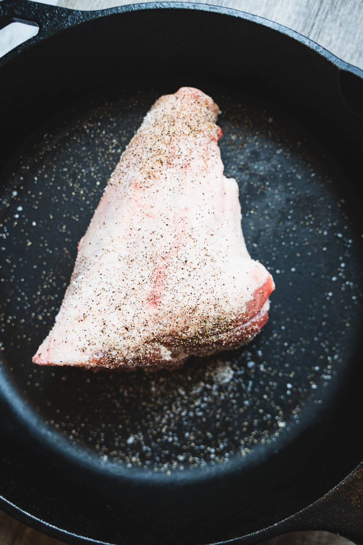 Lamb shank in cast iron skillet, seasoned with salt.