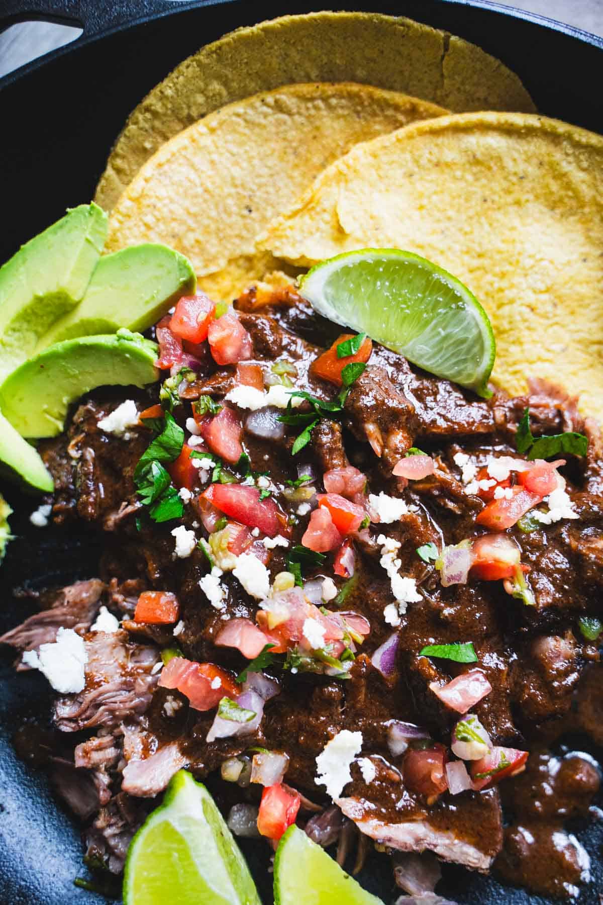 Barbacoa chipotle meat shredded and garnished with tomatoes, onions, cilantro, slices of lime and corn tortillas.
