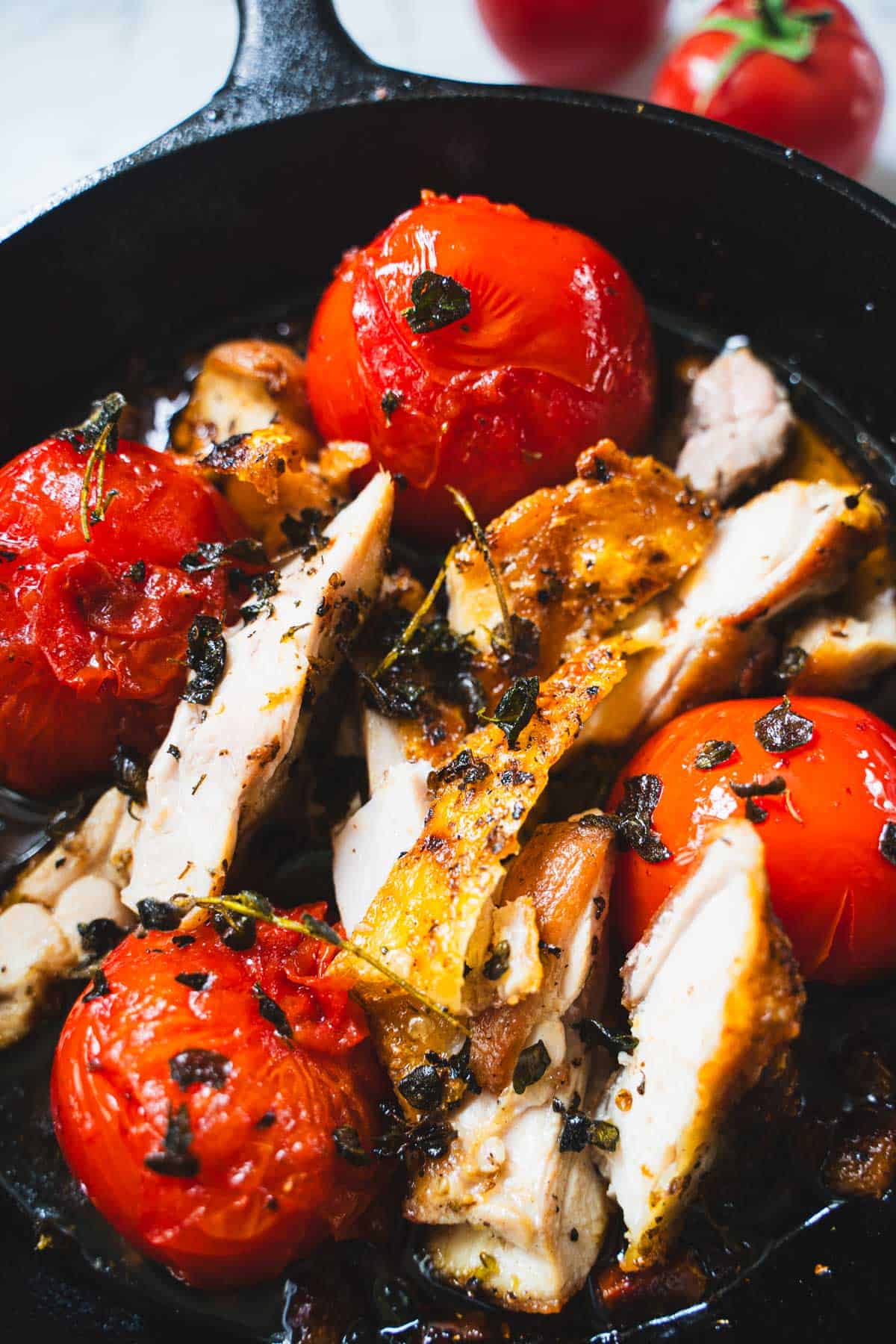 Pan fried chicken and pan fried tomatoes in a cast iron skillet sprinkled with crispy oregano.