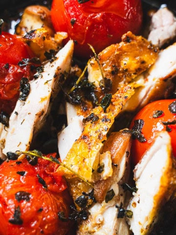 Pan fried chicken and pan fried tomatoes in a cast iron skillet sprinkled with crispy oregano.