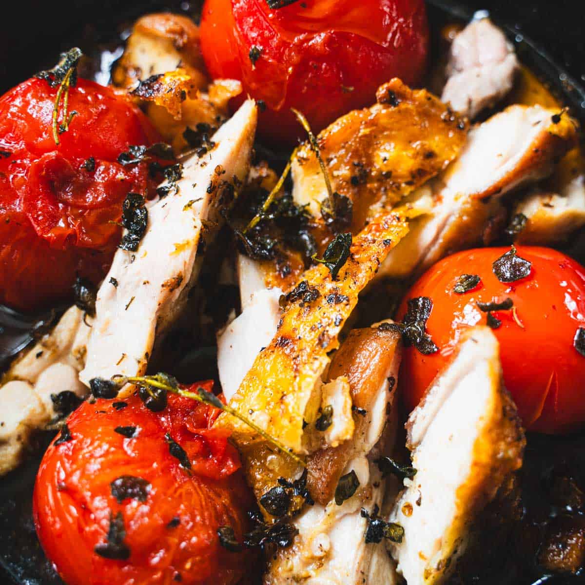 Pan fried chicken and pan fried tomatoes in a cast iron skillet sprinkled with crispy oregano.