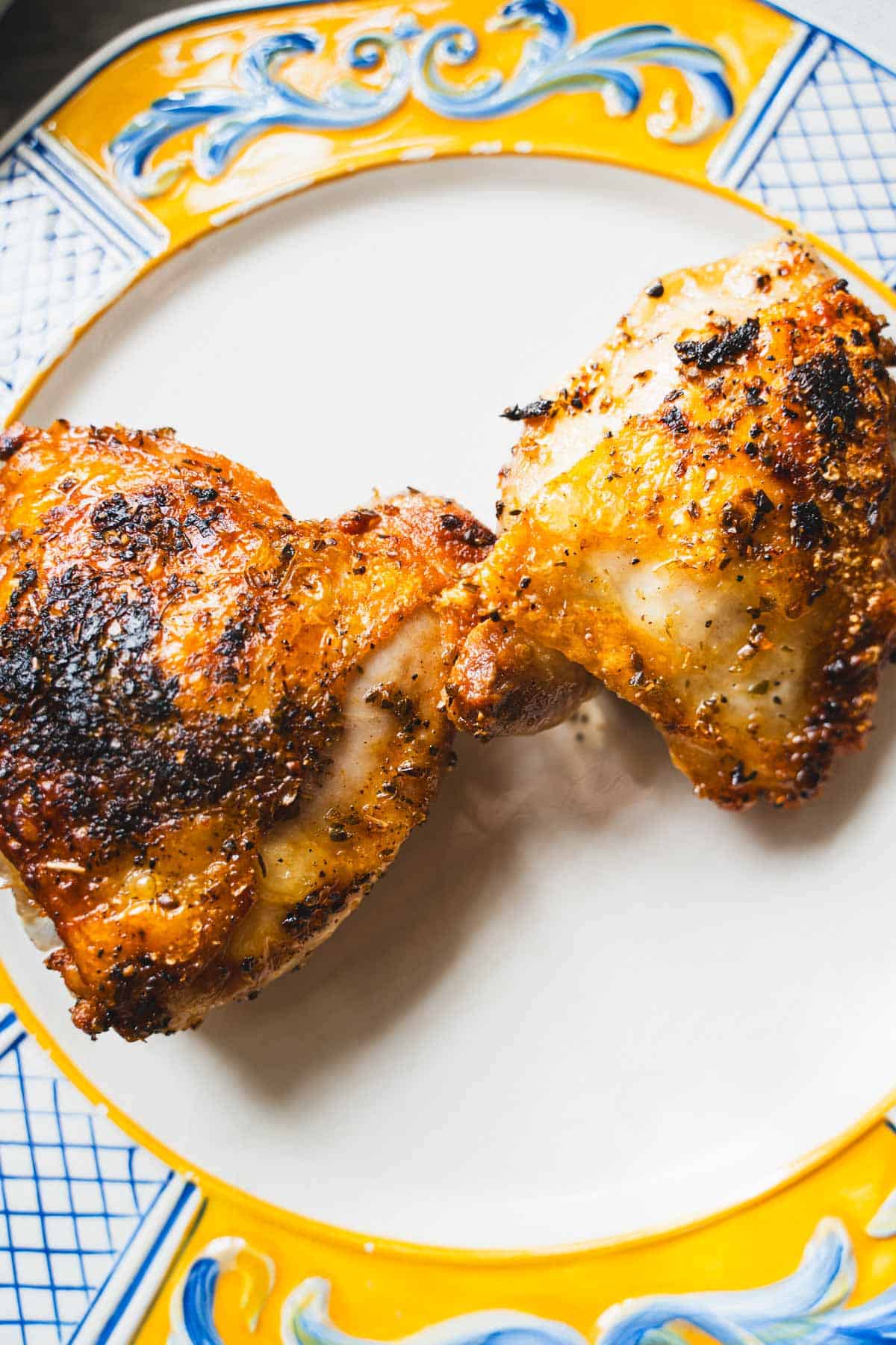pan fried chicken thighs resting on a white plate with yellow and blue border.