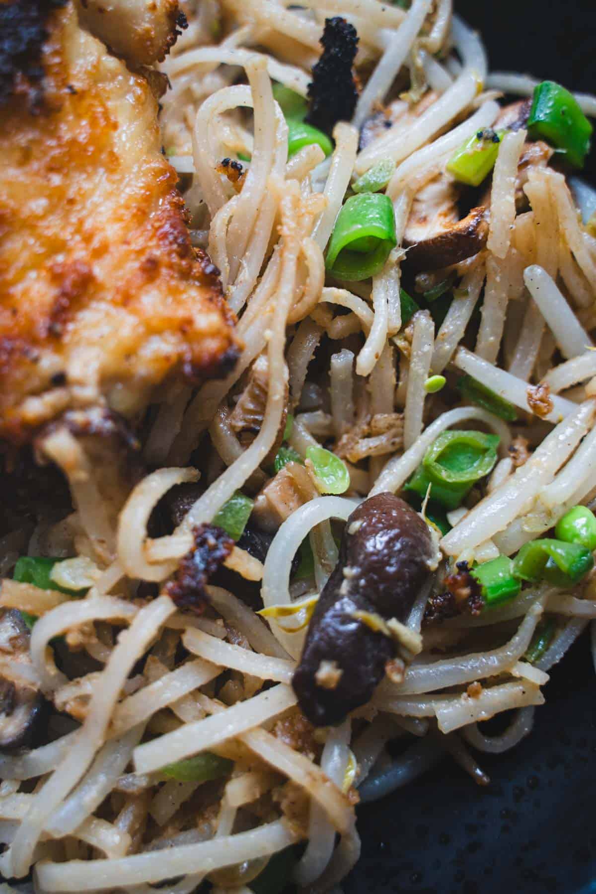 Sheet Pan Miso Chicken plated on a bed of pan fried glass noodle salad on a black plate.
