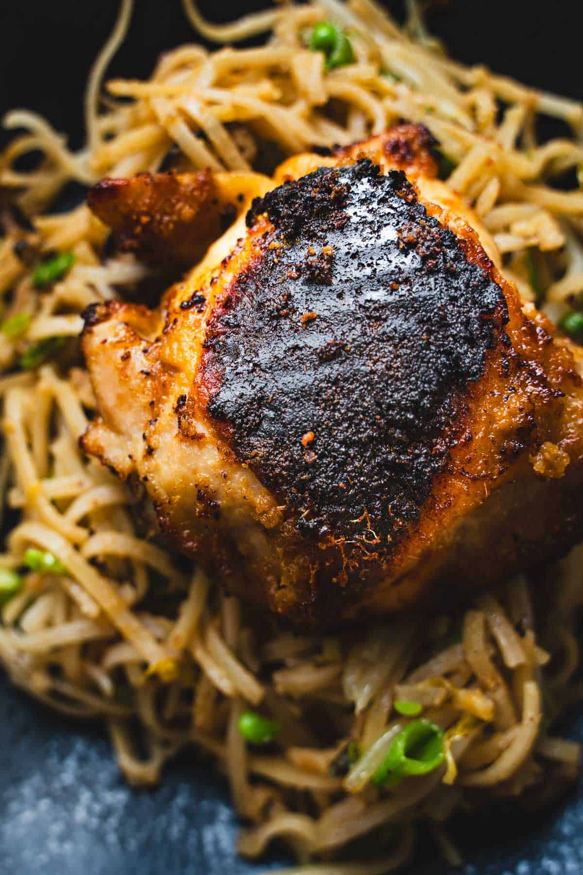 MIso chicken on a bed of pan fried glass noodles on a black plate.