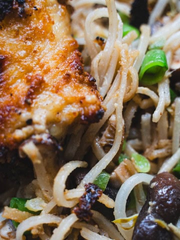 Sheet Pan Miso Chicken plated on a bed of pan fried glass noodle salad on a black plate.