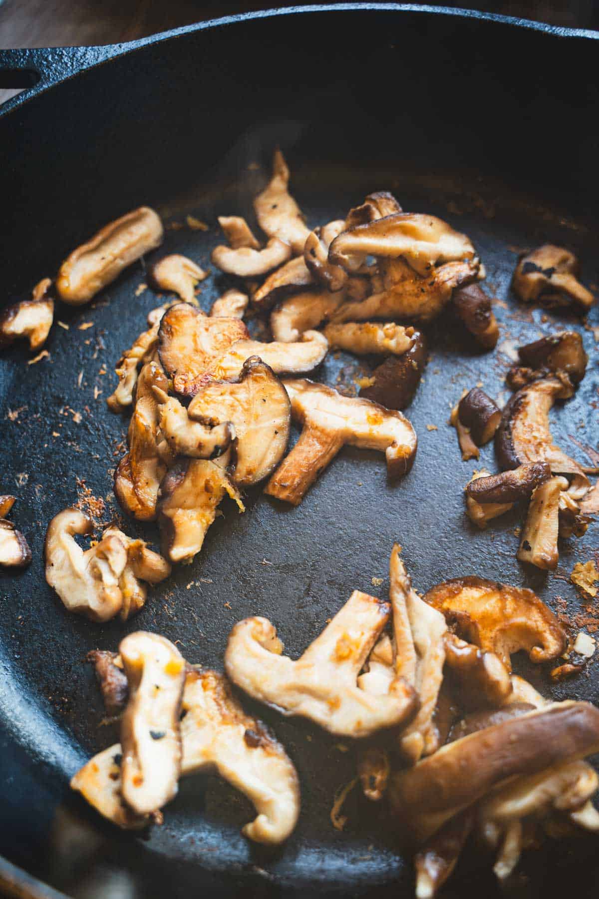 Mushrooms cooking in black cast iron skillet to make a pan fried noodle salad.