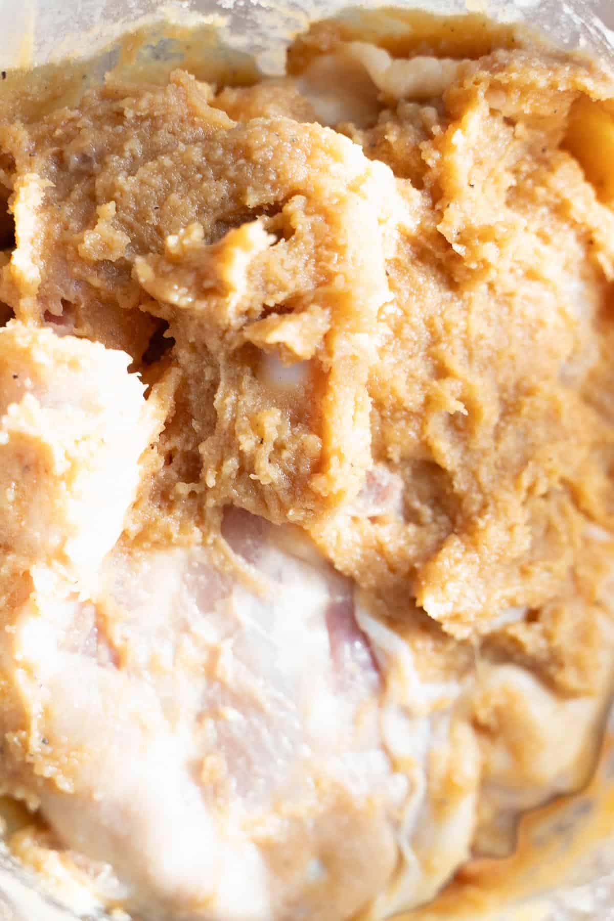 Chicken thighs and miso marinade in a clear glass bowl to make Miso Chicken.