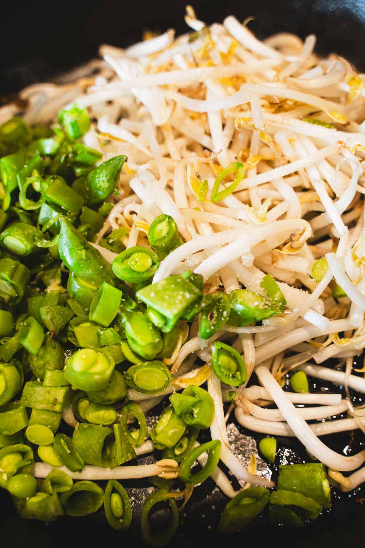 Bean sprouts and snap peas in black cast iron skillet to make pan fried noodle salad.