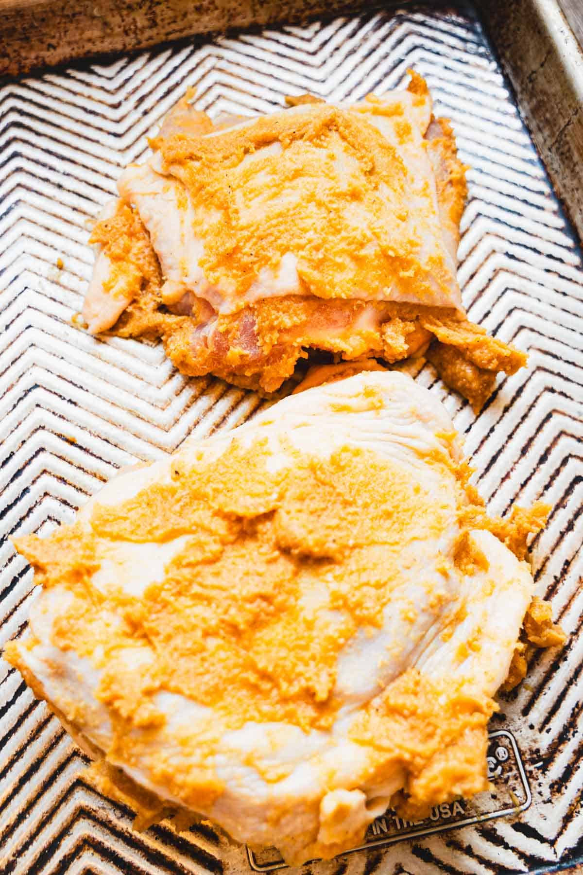 2 chicken thighs massaged with miso marinade on a sheet pan.