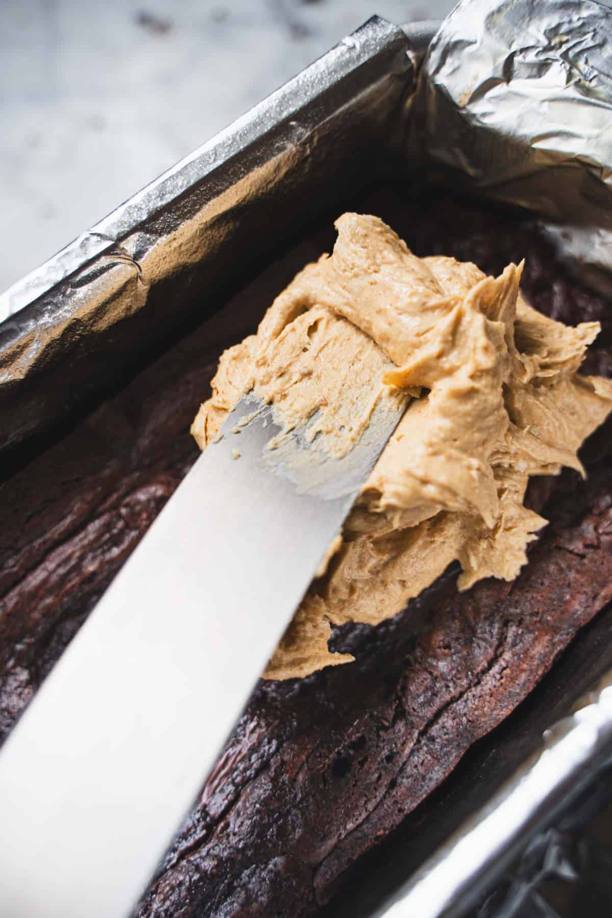 Spreading biscoff cookie butter buttercream on top of the brownie base with a off set spatula.
