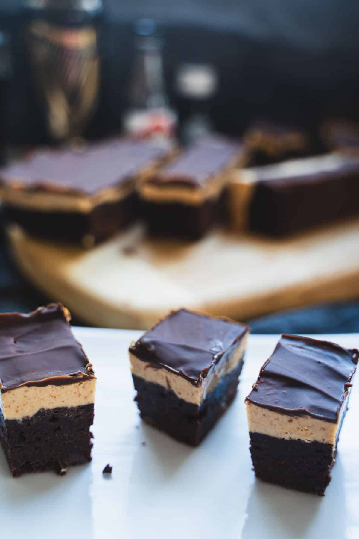 Bourbon biscoff cookie butter brownies on a marble serving platter with variations of alcohol in the background.