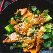 Dumpling Potsticker dinner with smashed cucumber and carrot salad drizzled with asian peanut sauce and sesame seeds in a block bowl with red chop sticks.
