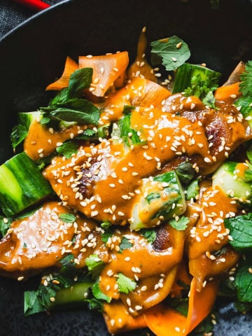 Dumpling Potsticker dinner with smashed cucumber and carrot salad drizzled with asian peanut sauce and sesame seeds in a block bowl with red chop sticks.