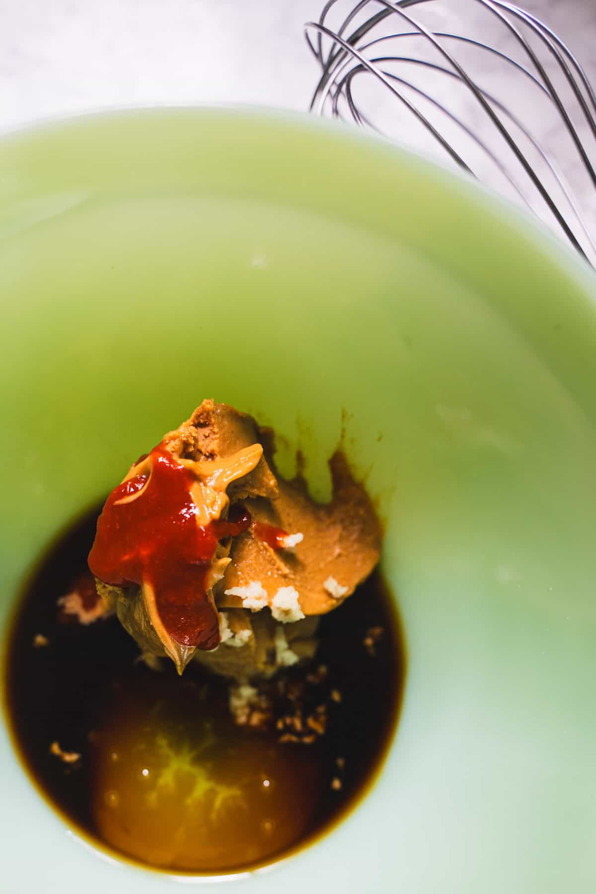 Soy sauce, rice vinegar, honey and chili crisp in green bowl to make asian peanut sauce.