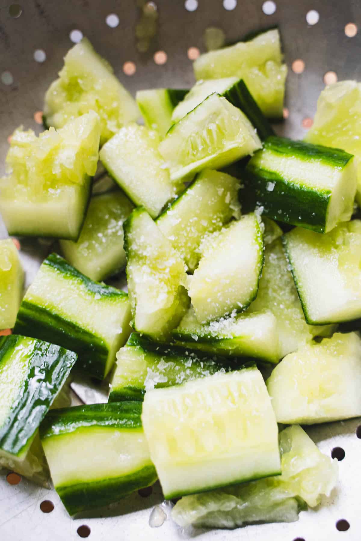 Salted smashed cucumber pieces in colonder for smashed cucumber salad.