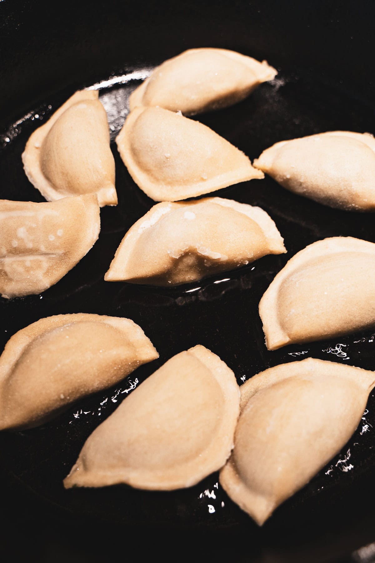 Frozen dumpling potstickers in hot oil in a black cast iron skillet.