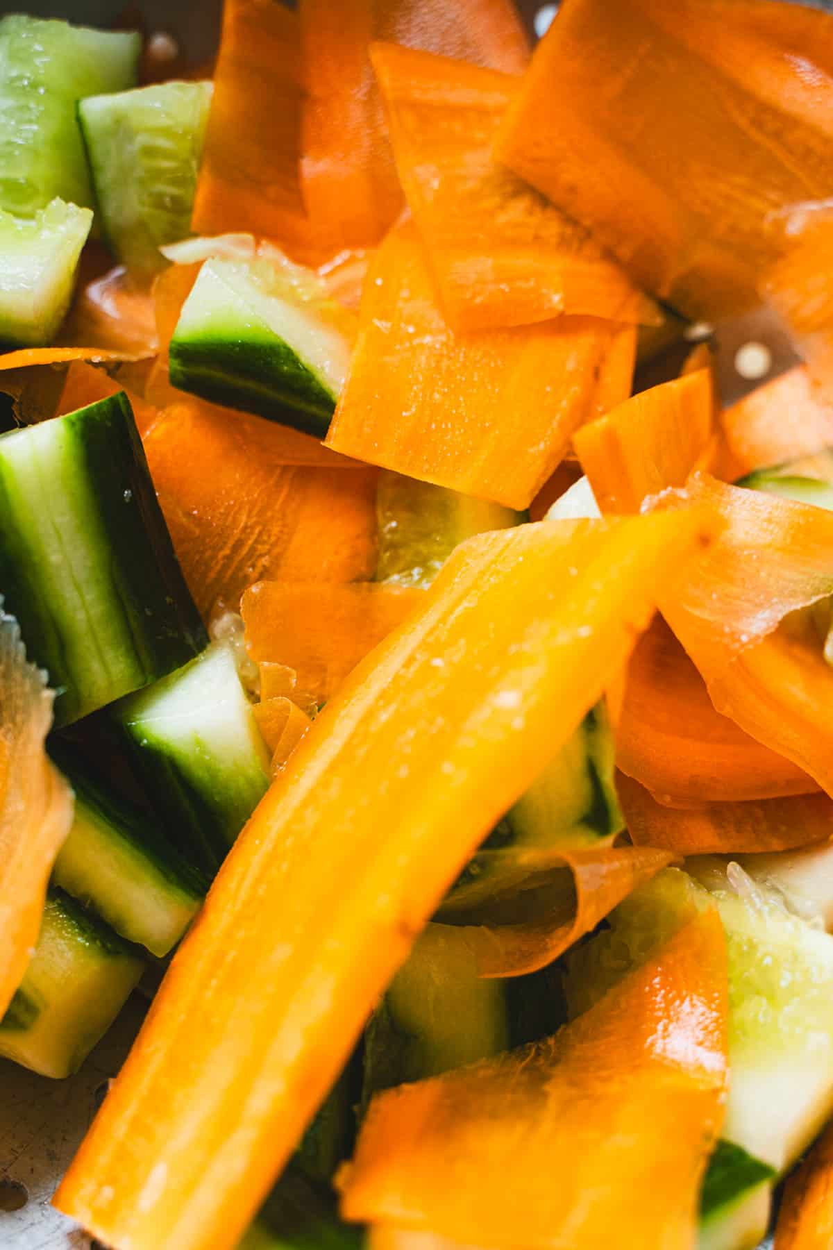 Carrot ribbons in a colander with smashed cucumbers to make a smashed cucumber and carrot salad.