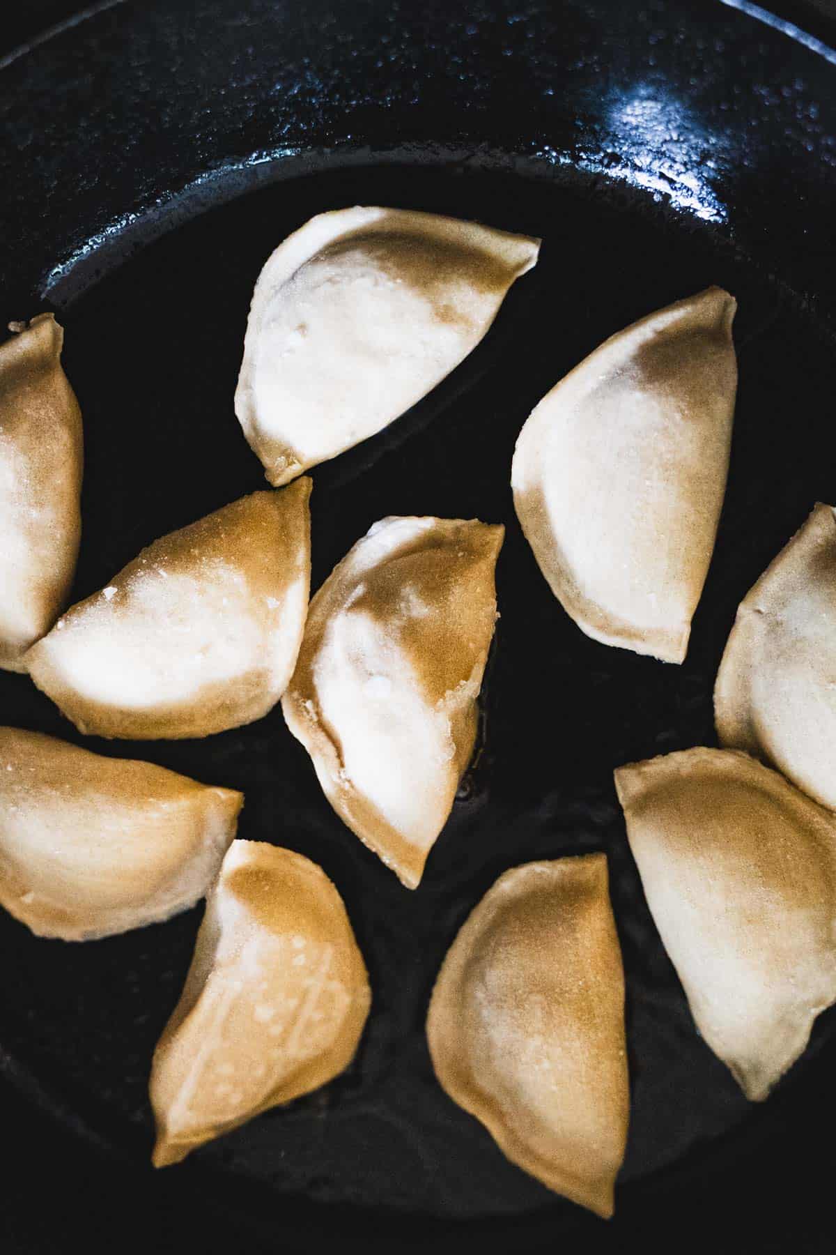 Frozen dumpling potstickers in cast iron skillet.