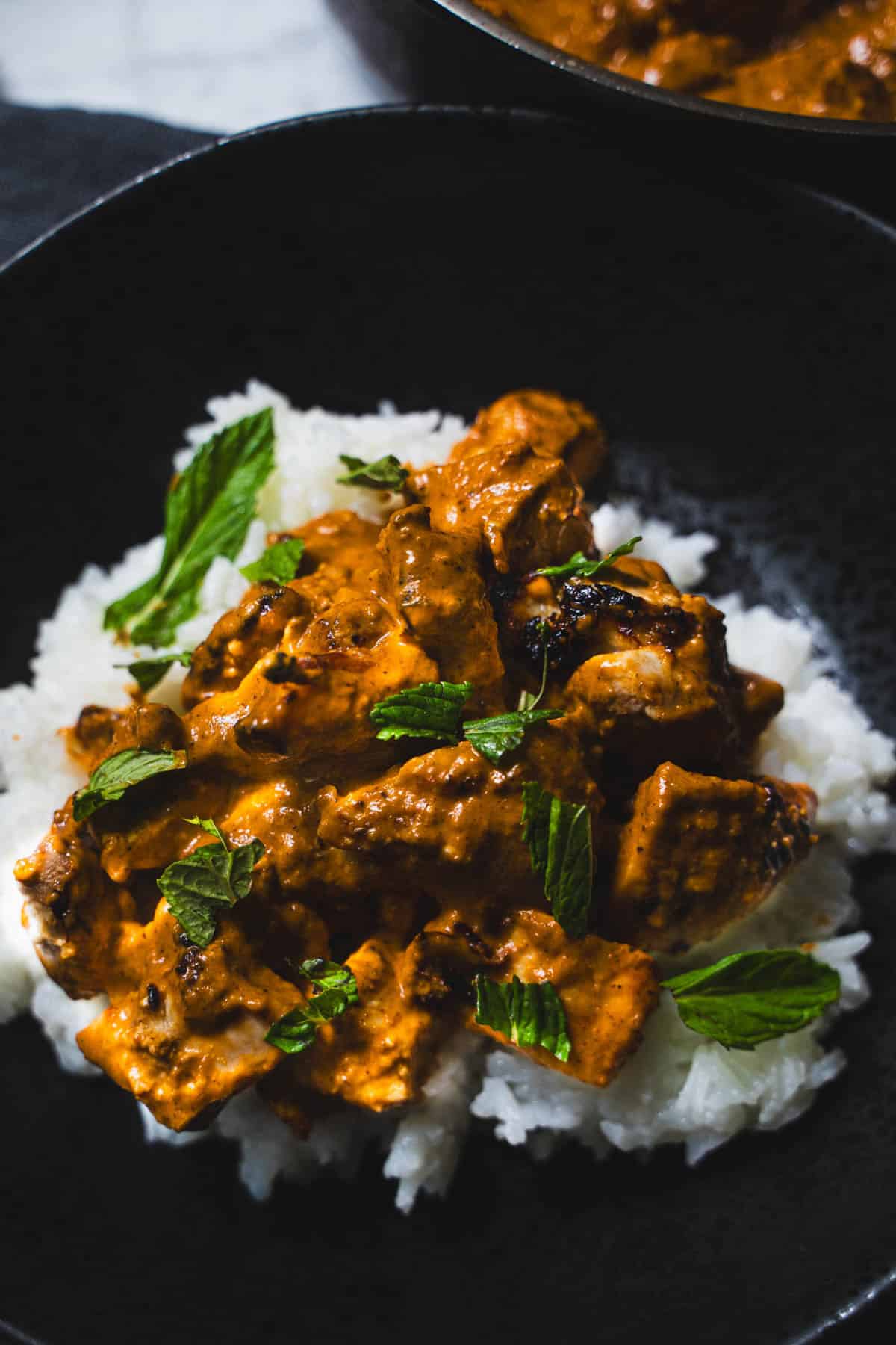 Butter chicken served over rice in a black bowl.