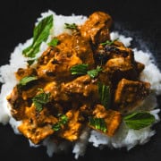 Butter chicken served over rice in a black bowl.