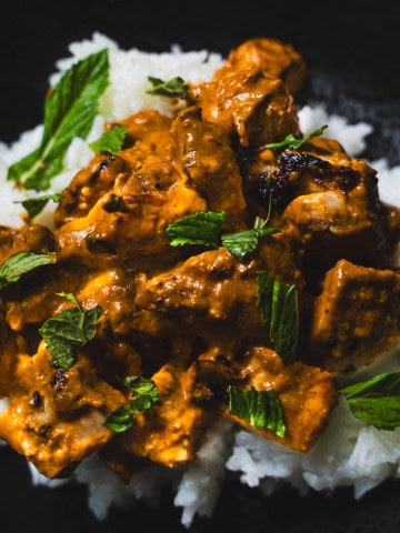 Butter chicken served over rice in a black bowl.