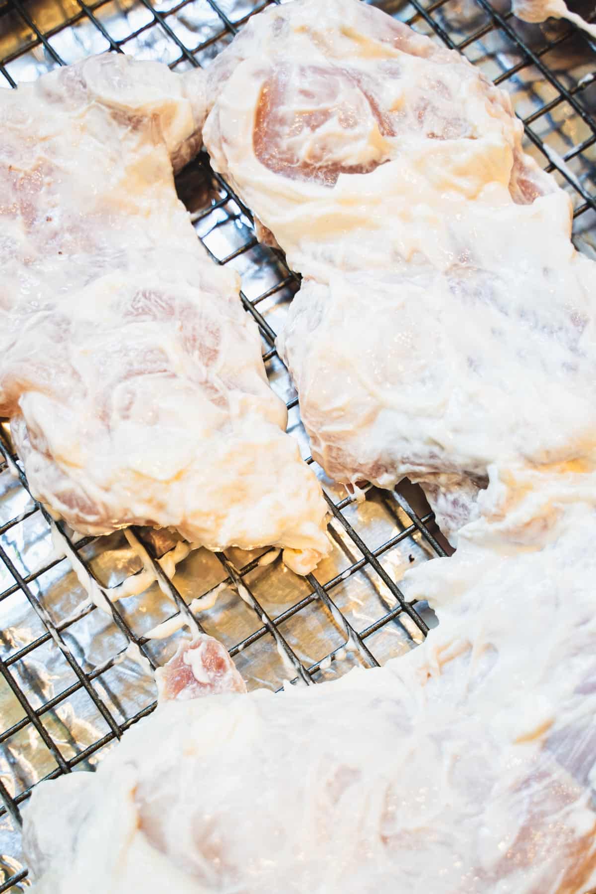 Yougurt coated chicken thighs on a wire rack inserted inside baking sheet.