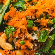 Raw shredded carrots tossed with cilantro, cashews and seasonings in a white bowl.