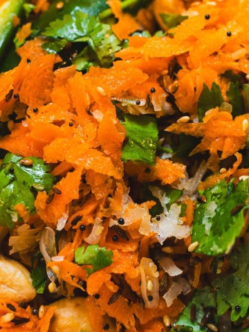 Raw shredded carrots tossed with cilantro, cashews and seasonings in a white bowl.