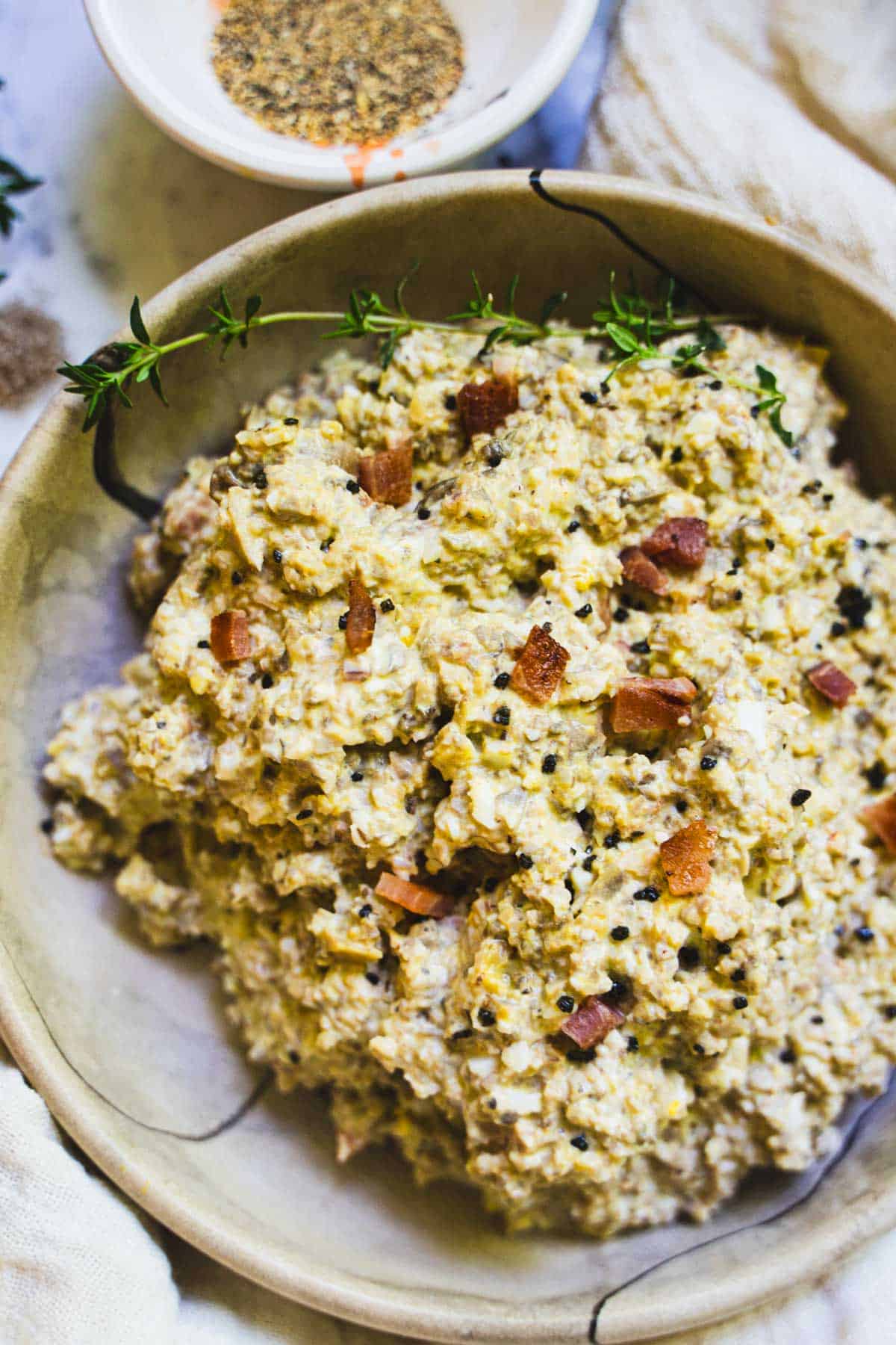 Mushroom salad in a tan bowl garnished with bacon bits and black salt.