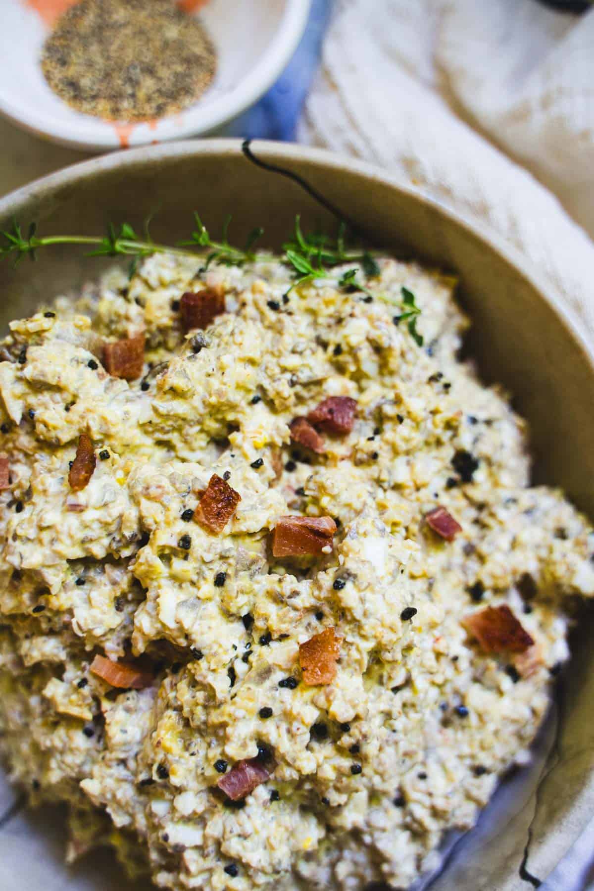 Mushroom salad in a tan bowl garnished with bacon bits and black salt.