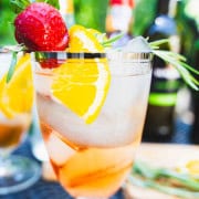 Rose port and tonic in a balloon wine glass with ice and a garnish of rosemary, orange and strawberry on resting over the lip of the glass.