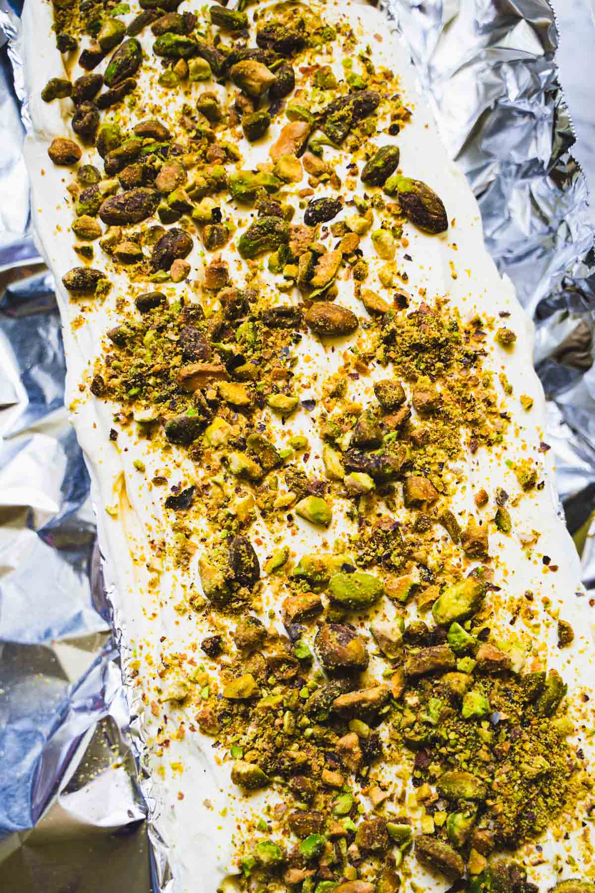 Pistachios spread on top of kulfi cardamom ice cream in a foil lined tart pan.