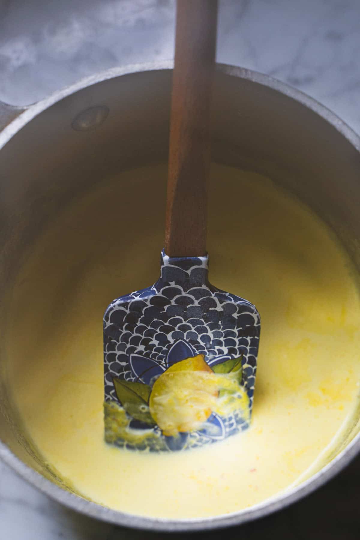 Saffron infused cream in a sauce with a blue and yellow spatula.